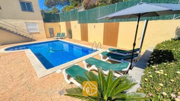 Piscina exterior privada en Villa Holiday, rodeada de tumbonas verdes, una sombrilla oscura y suelo de patio de piedra.