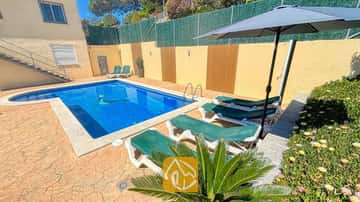Piscina exterior privada en Villa Holiday, rodeada de tumbonas verdes, una sombrilla oscura y suelo de patio de piedra.