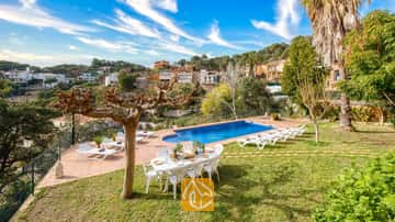 Piscina privada en Villa Marysol rodeada de una terraza de losas, césped, mesa de comedor con sillas y tumbonas, con el telón de fondo de una colina.