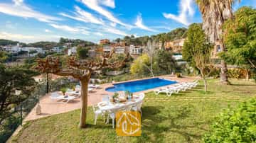 Piscina privada en Villa Marysol rodeada de una terraza de losas, césped, mesa de comedor con sillas y tumbonas, con el telón de fondo de una colina.
