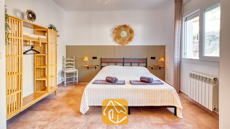 Dormitorio con una cama doble que incluye toallas enrolladas, cabecero de listones de madera, armario de bambú y suelo de baldosas.