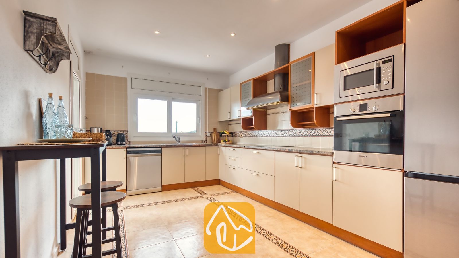 Cocina con gabinetes de color beige claro, electrodomésticos de acero inoxidable y pisos de loseta en Villa Ibiza.