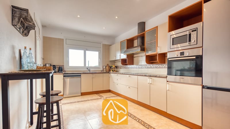 Cocina con gabinetes de color beige claro, electrodomésticos de acero inoxidable y pisos de loseta en Villa Ibiza.
