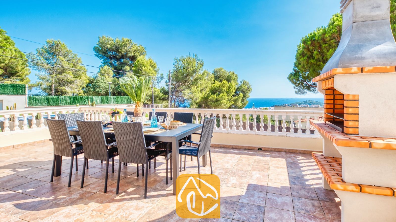 Terraza de Villa Ibiza con mesa de comedor al aire libre y sillas de mimbre negro, barbacoa de obra integrada y vistas al mar.
