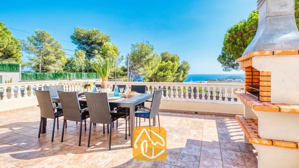 Terraza de Villa Ibiza con mesa de comedor al aire libre y sillas de mimbre negro, barbacoa de obra integrada y vistas al mar.