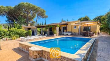 Piscina privada y exterior amarillo de Villa Iako, que cuenta con pavimento de piedra, tumbonas y una zona de comedor al aire libre bajo una sombrilla contra un cielo azul despejado.