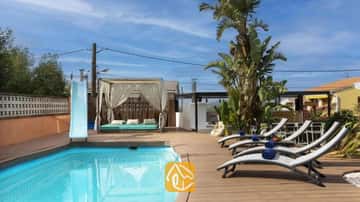 Piscina privada con tobogán azul, terraza de madera, tumbonas grises con toallas azules y una cabaña con cortinas en Villa Soleia.