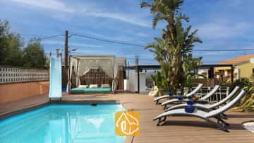 Piscina privada con tobogán azul, terraza de madera, tumbonas grises con toallas azules y una cabaña con cortinas en Villa Soleia.
