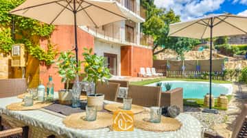 Mesa de comedor exterior decorada con individuales de mimbre, vasos de cristal y limoneros en maceta en Villa Sunny Beach, con vistas a una piscina y terraza.