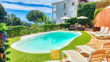 Piscina privada con tumbonas y zona de estar al aire libre en Villa Sunny Beach, España, que cuenta con un césped verde, sombrillas blancas y vistas al mar al fondo.